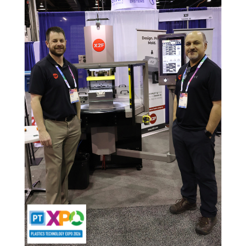 Two X2F team members standing beside the E60Vi machine at PTXPO 2026